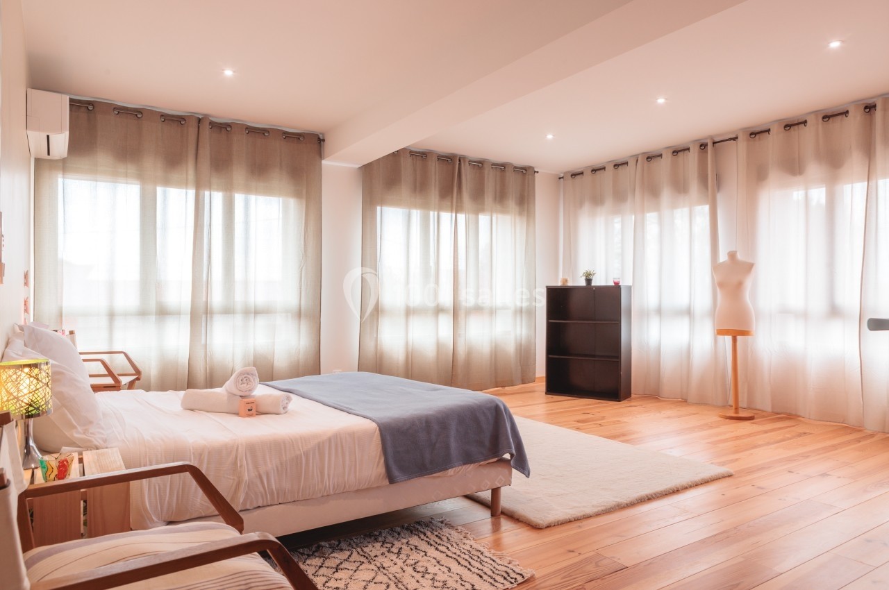 Chambre lumineuse avec lit double, parquet en bois, rideaux translucides, étagère noire et mannequin de couture.