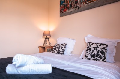 Lit double avec draps blancs, coussins décoratifs noirs et blancs, lampe de chevet allumée et tableau mural coloré.