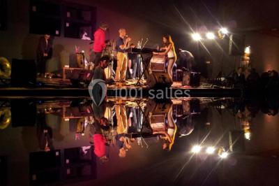 Lit double avec draps blancs, coussins décoratifs noirs et blancs, lampe de chevet allumée et tableau mural coloré.