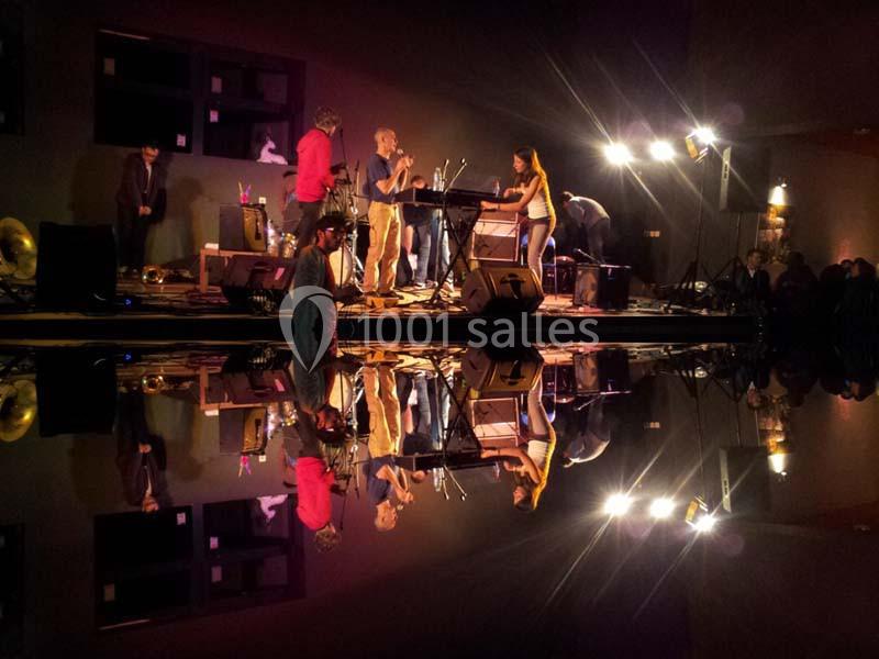 Un groupe de musiciens se produit sur scène avec des éclairages colorés, reflétés sur une surface brillante.