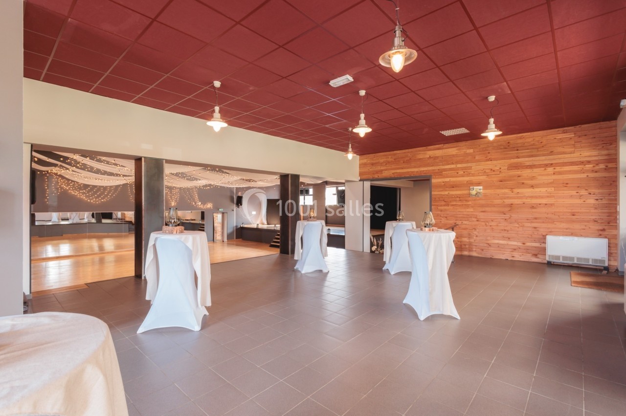 Salle de réception lumineuse avec tables hautes, guirlandes suspendues et murs en bois et carrelage au sol.