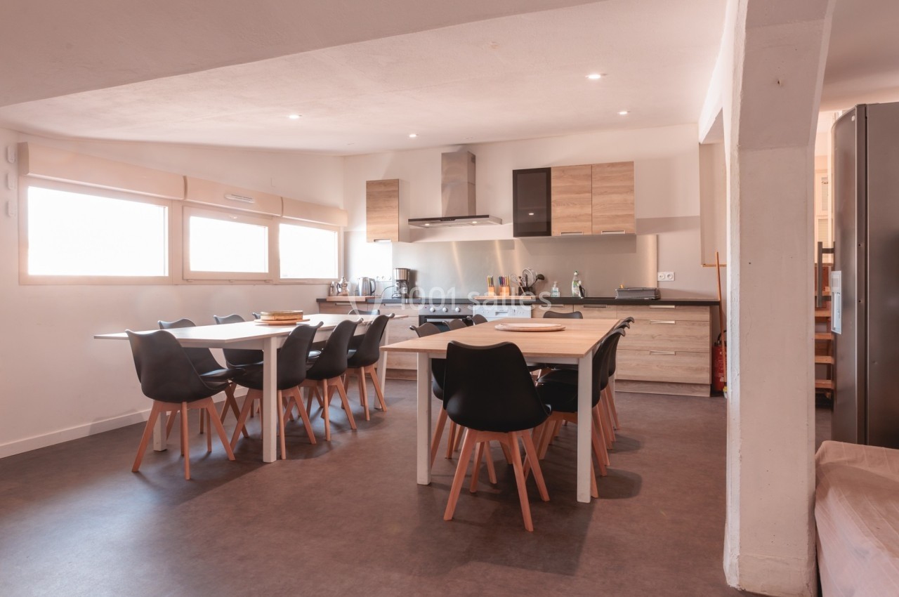 Cuisine moderne avec table à manger, chaises noires, meubles en bois clair et éclairage naturel.