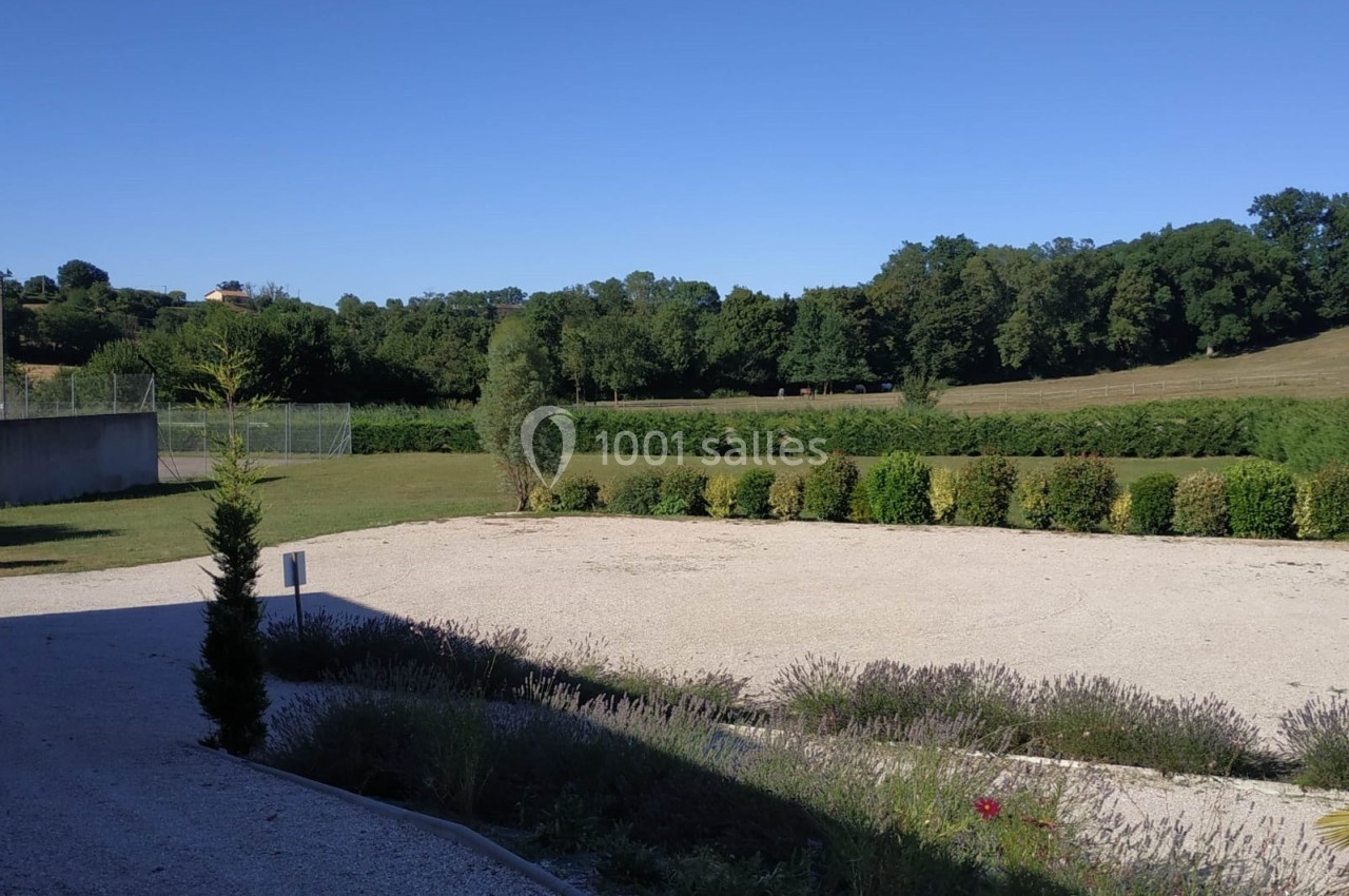 Vue d'un jardin avec allée gravillonnée, haies taillées, pelouse et arbres en arrière-plan sous un ciel dégagé.