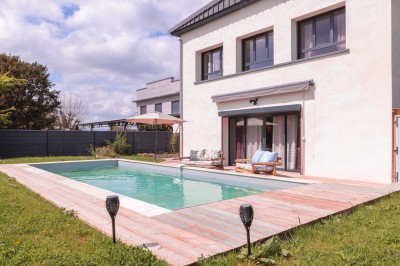 Vue d'un jardin avec allée gravillonnée, haies taillées, pelouse et arbres en arrière-plan sous un ciel dégagé.