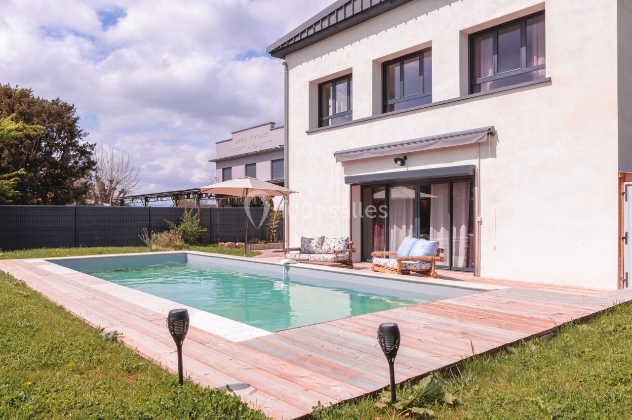 Maison moderne avec piscine extérieure entourée d'une terrasse en bois, jardin et mobilier de détente.