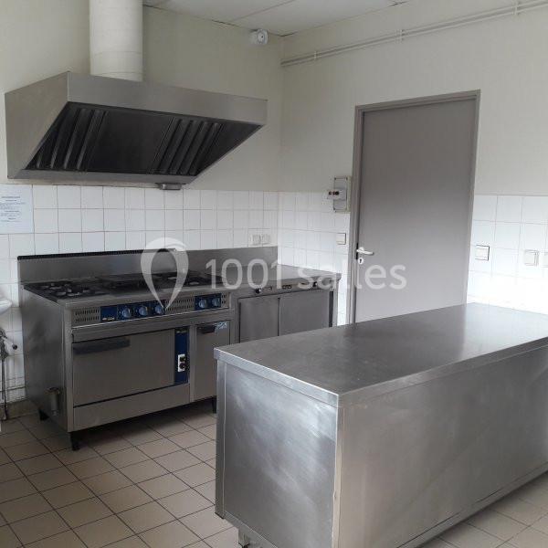 Cuisine professionnelle avec plan de travail en inox, cuisinière à gaz, hotte et carrelage mural blanc.