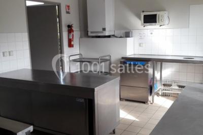 Cuisine professionnelle avec plan de travail en inox, cuisinière équipée et hotte, éclairée par une fenêtre.