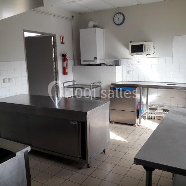 Cuisine professionnelle avec plans de travail en inox, micro-ondes, lave-vaisselle et équipement mural.