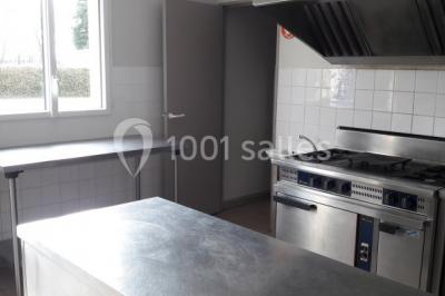 Cuisine professionnelle avec plan de travail en inox, cuisinière équipée et hotte, éclairée par une fenêtre.