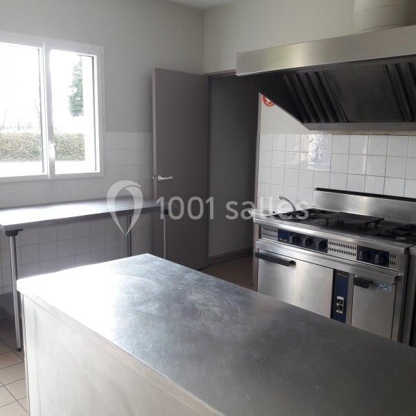 Cuisine professionnelle avec plan de travail en inox, cuisinière équipée et hotte, éclairée par une fenêtre.