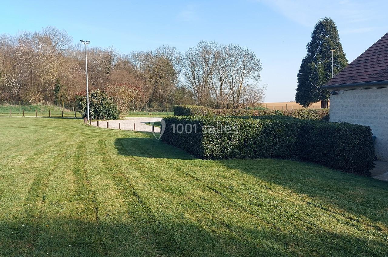 Pelouse tondue avec des haies taillées, un chemin gravillonné et des arbres en arrière-plan par temps clair.