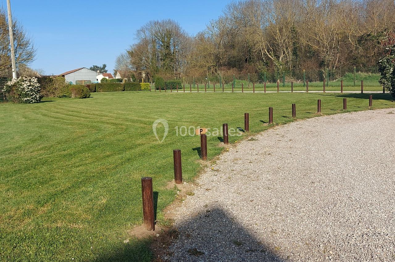 Pelouse bien entretenue bordée de poteaux en bois, avec un chemin gravillonné et des arbres en arrière-plan.