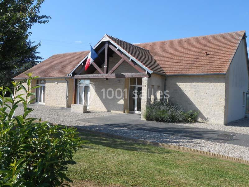 Bâtiment en pierre avec un toit en tuiles, drapeau français sur la façade, entouré de végétation et d'une allée gravillonnée.