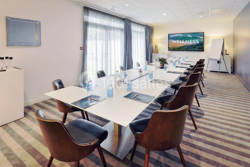 Salle de réunion lumineuse avec une grande table, chaises en bois, écran mural et matériel de conférence.