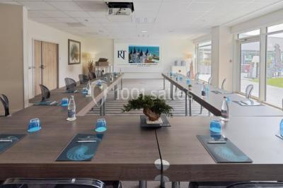 Salle de restaurant lumineuse avec tables dressées, chaises violettes, luminaires dorés et grandes baies vitrées.