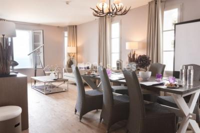 Salle de restaurant lumineuse avec tables dressées, chaises violettes, luminaires dorés et grandes baies vitrées.