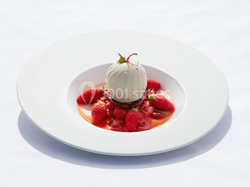 Dessert composé d'une boule de glace vanille sur un lit de fraises fraîches et de coulis, présenté dans une assiette blanche.