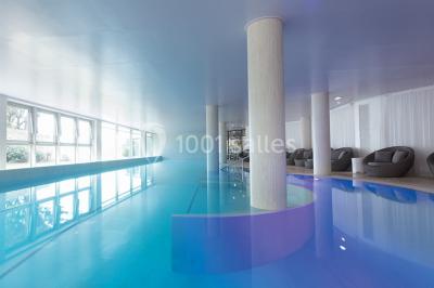 Salle de restaurant lumineuse avec tables dressées, chaises violettes, luminaires dorés et grandes baies vitrées.