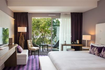 Salle de restaurant lumineuse avec tables dressées, chaises violettes, luminaires dorés et grandes baies vitrées.