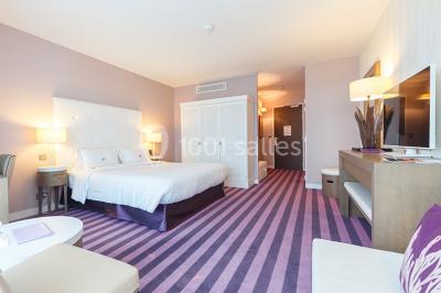 Salle de restaurant lumineuse avec tables dressées, chaises violettes, luminaires dorés et grandes baies vitrées.