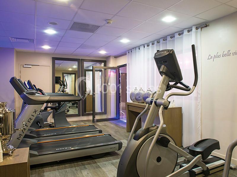 Salle de sport équipée de tapis de course et d'un vélo elliptique, éclairée par une lumière douce.