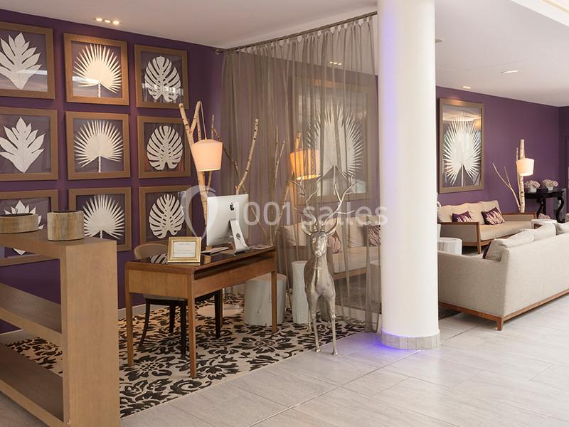 Espace d'accueil avec bureau en bois, fauteuils, décoration murale de feuilles encadrées et éclairage chaleureux.