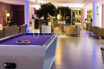 Salle de restaurant lumineuse avec tables dressées, chaises violettes, luminaires dorés et grandes baies vitrées.