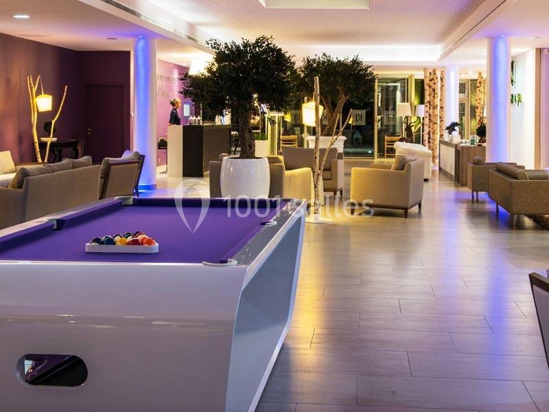 Salle moderne avec un billard violet au premier plan, entourée de fauteuils et éclairée par des lumières tamisées.