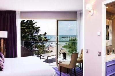 Salle de restaurant lumineuse avec tables dressées, chaises violettes, luminaires dorés et grandes baies vitrées.