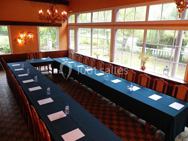 Salle de réunion lumineuse avec deux longues tables alignées, chaises en bois, bouteilles d'eau et papiers disposés.
