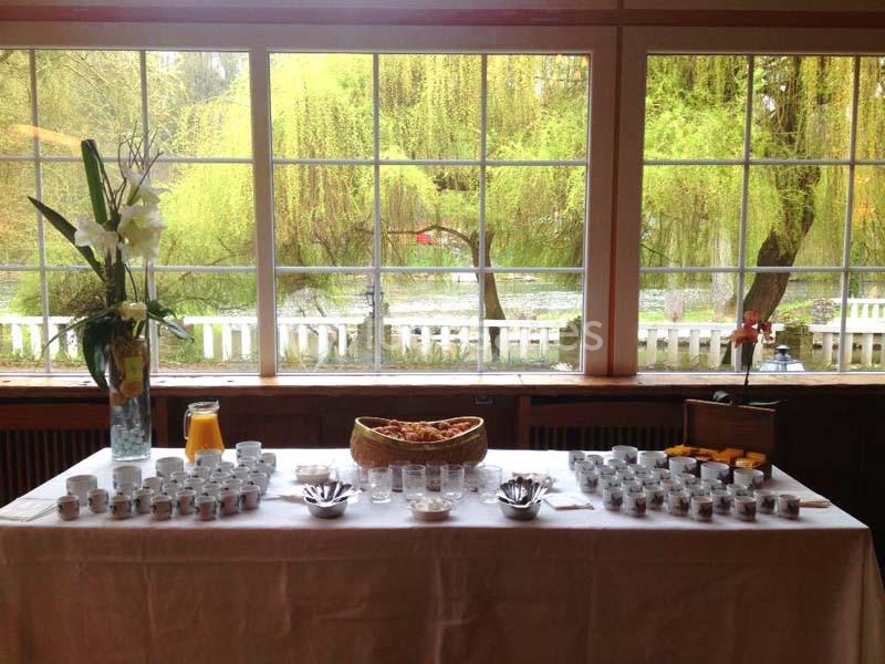 Table dressée avec des verrines, une carafe de jus d'orange et un vase de fleurs, devant une grande baie vitrée donnant sur…