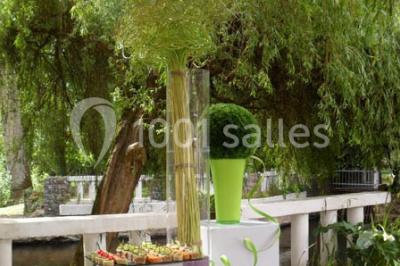 Table décorée en extérieur avec des amuse-bouches, un vase de fleurs hautes et des éléments végétaux sous un arbre.