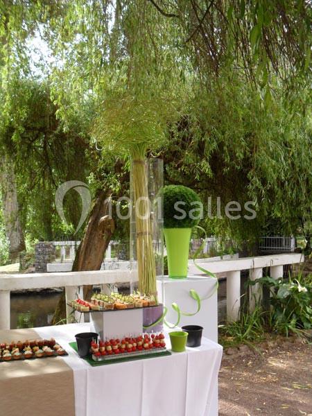 Table décorée en extérieur avec des amuse-bouches, un vase de fleurs hautes et des éléments végétaux sous un arbre.