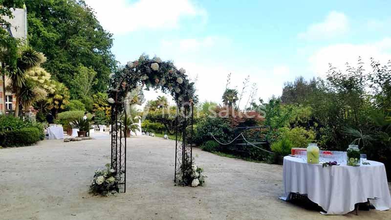 Arche fleurie dans un jardin, entourée de tables dressées pour un événement en plein air.