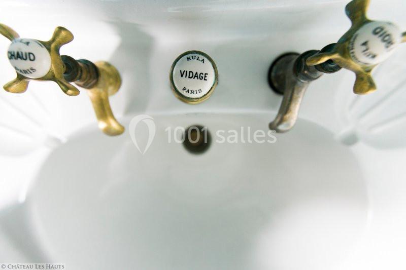 Robinetterie ancienne en laiton avec inscriptions ’chaud’, ’froid’ et ’vidage’, au-dessus d'un lavabo blanc.