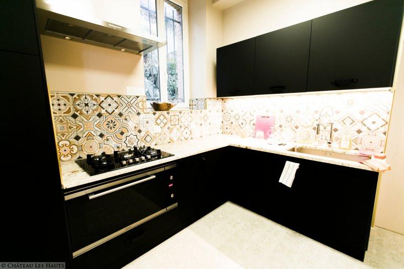 Cuisine moderne avec meubles noirs, plan de travail clair, crédence en carreaux décoratifs et fenêtre laissant entrer la…