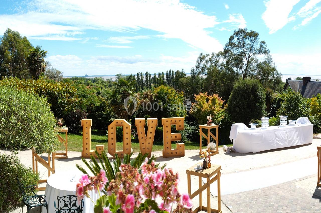 Vue panoramique d'un jardin ensoleillé avec des tables dressées et des lettres lumineuses formant le mot ’LOVE’.