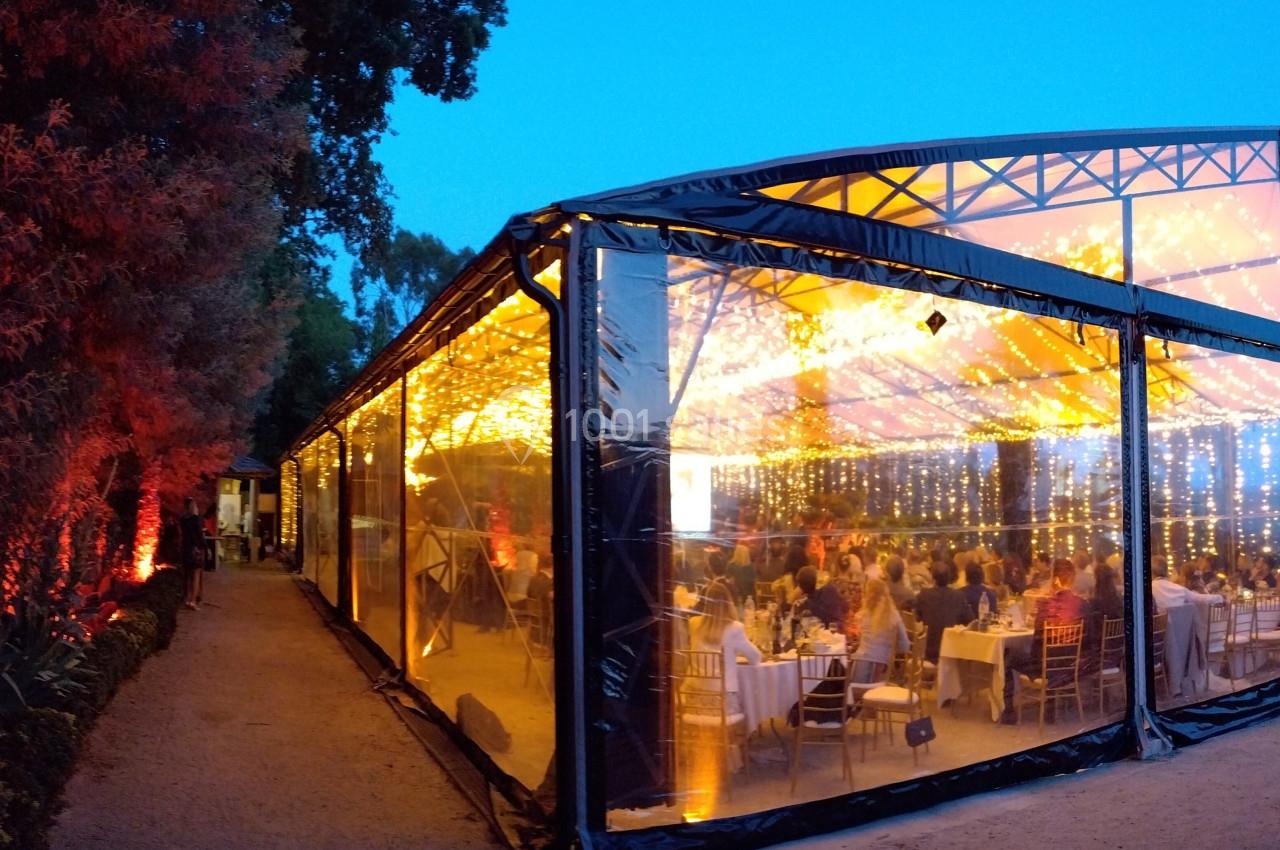 Vue extérieure d'une tente transparente illuminée, abritant un dîner festif en soirée.