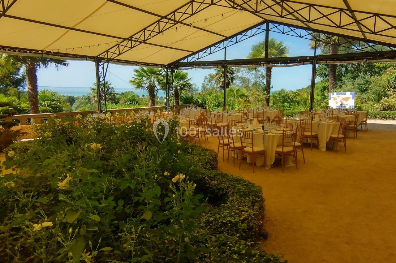 Salle extérieure couverte avec des tables dressées pour un événement, entourée de verdure et offrant une vue dégagée.