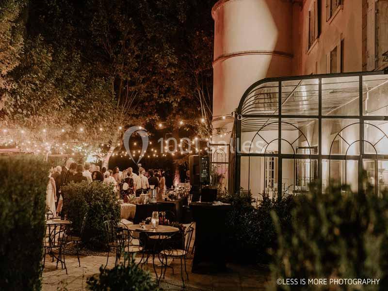Cour extérieure éclairée par des guirlandes lumineuses, avec des tables et des invités réunis en soirée.