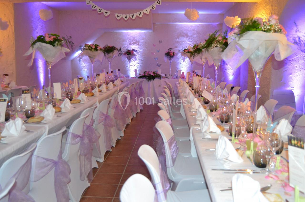 Salle de réception décorée pour un mariage, avec tables alignées, nappes blanches et ornements floraux.