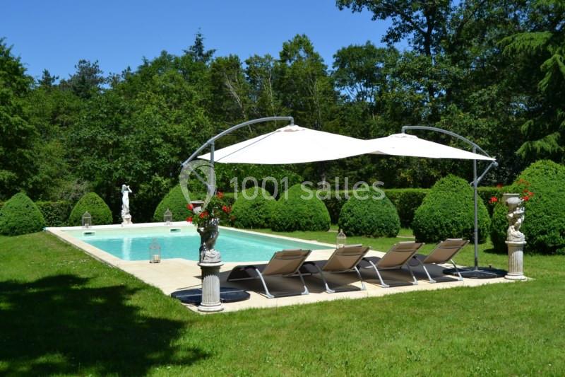 Piscine extérieure entourée de verdure, avec transats alignés et parasols blancs pour l'ombre.