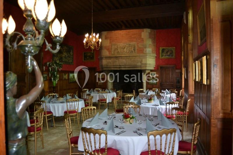 Salle de réception avec tables dressées, chaises dorées, cheminée en pierre et décorations murales classiques.