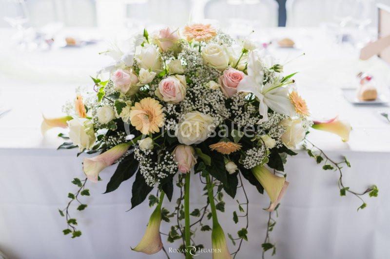 Bouquet de fleurs composé de roses, lys, gypsophiles et feuillage, disposé sur une table blanche.
