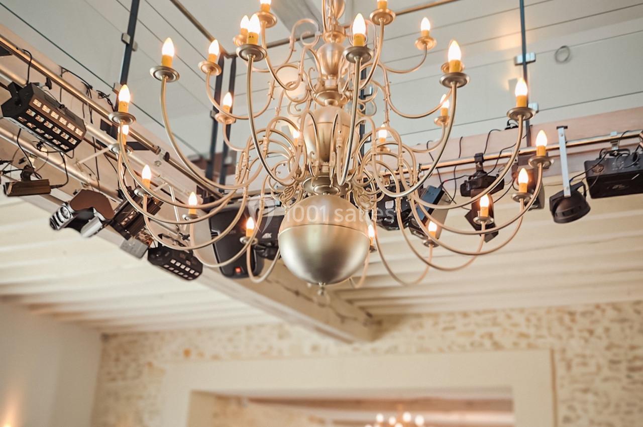 Lustre en métal avec ampoules allumées suspendu dans une grande salle lumineuse aux murs en pierre apparente.