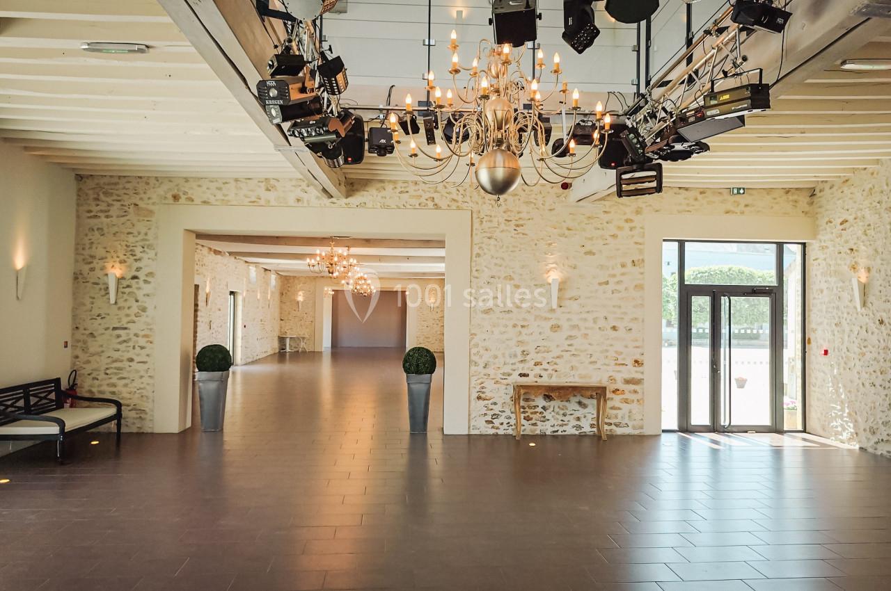 Salle spacieuse avec murs en pierre, lustres suspendus, éclairages techniques et grandes portes vitrées.