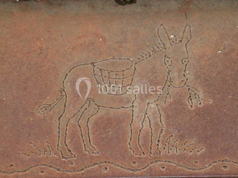 Gravure d'un âne portant des paniers sur une plaque de métal rouillée.