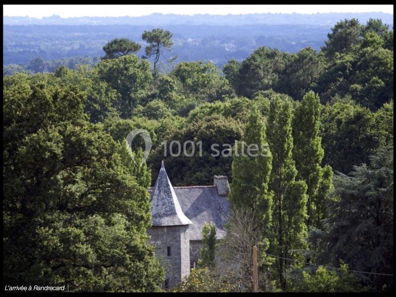 Vue d'un bâtiment en pierre avec une tour au milieu d'une forêt dense et un horizon dégagé en arrière-plan.
