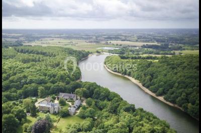 Paysages naturels avec lac entouré de forêts, sentiers boisés et ponton au bord de l'eau sous un ciel partiellement nuageux.