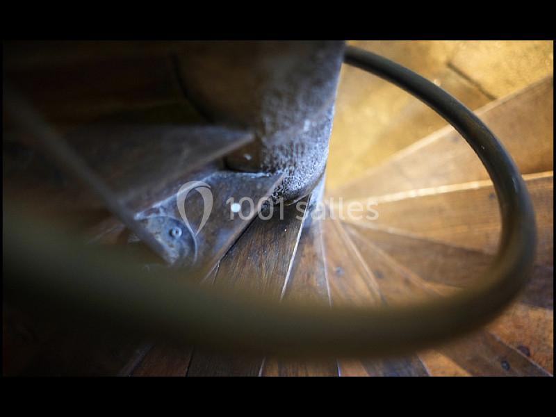 Escalier en colimaçon en bois vu de haut, avec une rampe métallique et des détails de texture usée.